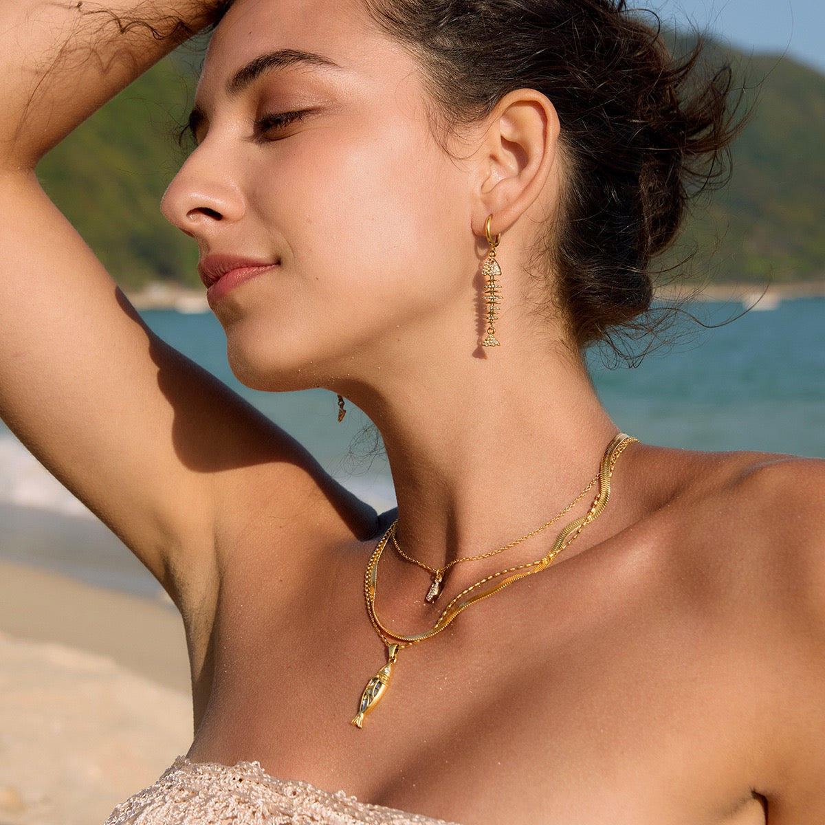 Gold-toned jewelry set featuring abalone shell accents, including a necklace and matching earrings, worn by a woman at the beach.