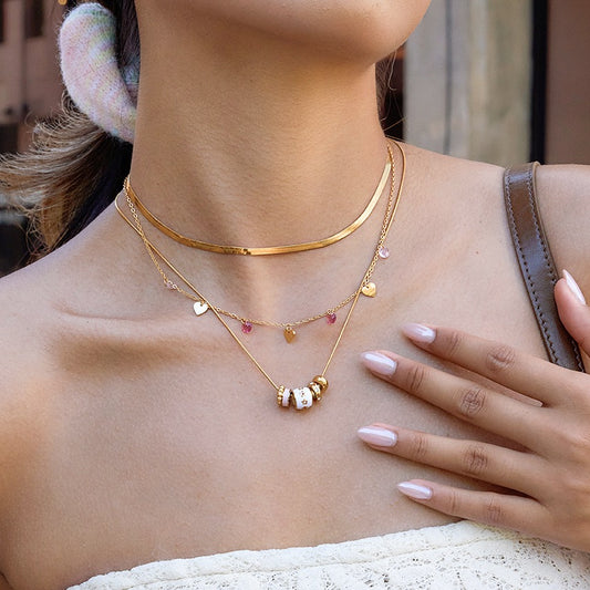 Gold layered necklaces with small heart and bead charms, worn on a woman's neck and chest area.