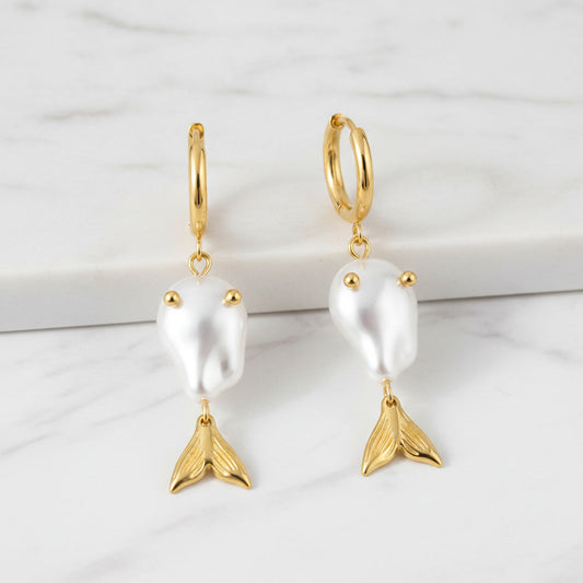 Esta Sirena Gemini 2.5 luxury gold earrings on white marble surface, showcasing elegant, polished gold jewelry with intricate design details.